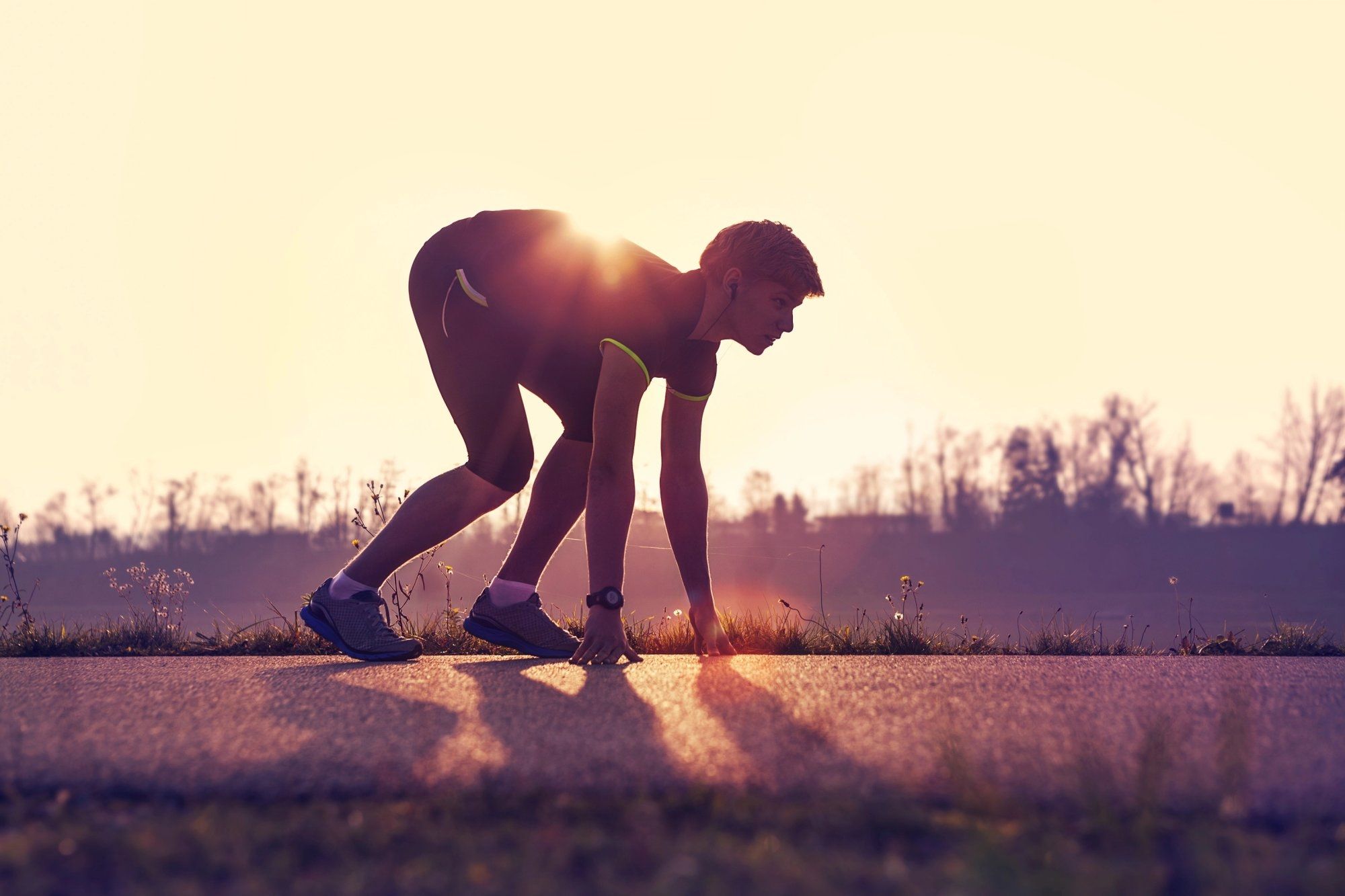A runner stands in the starting position to begin his run at dusk.