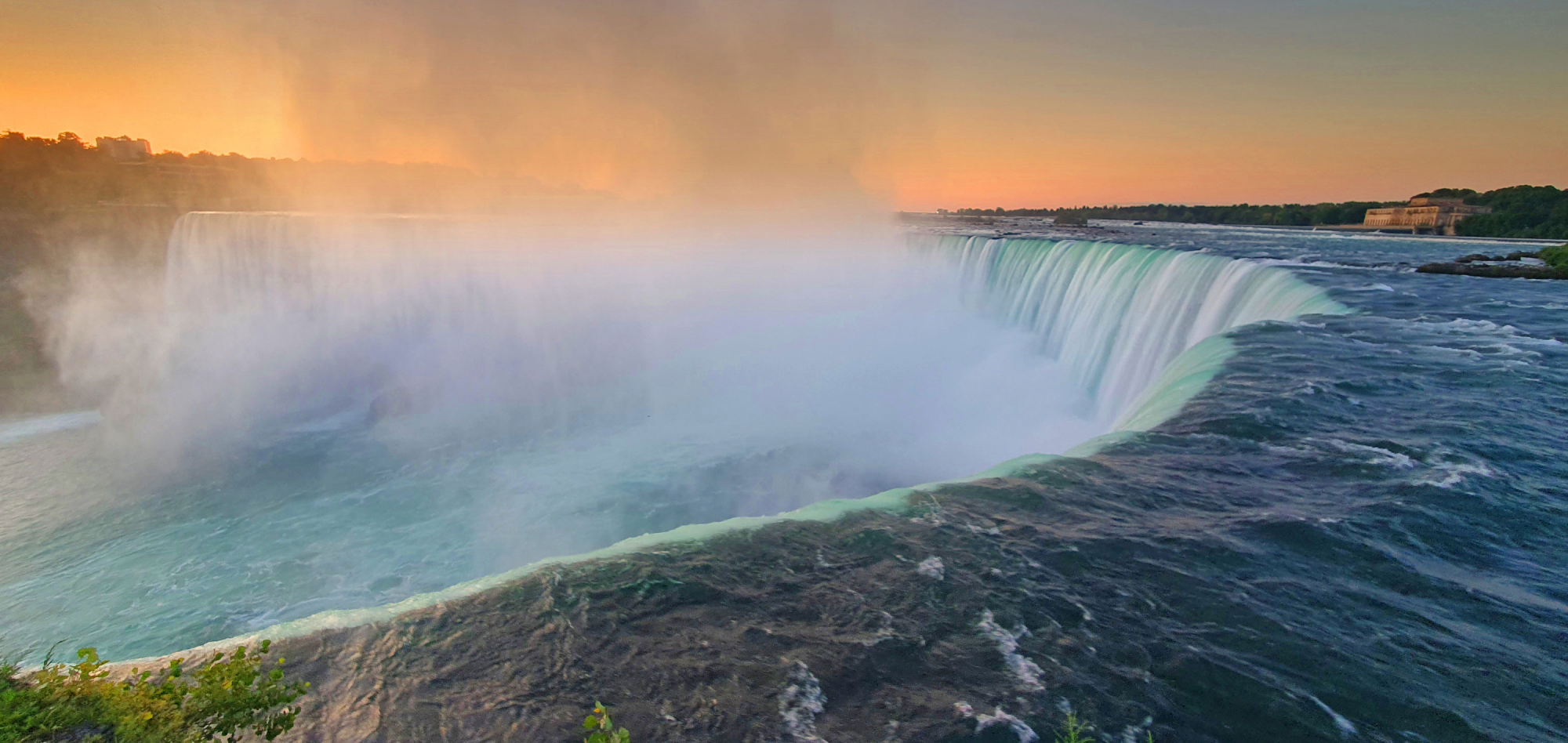 A breathtaking view of Niagara Falls in the warm light of sunset – mist rises and catches the ligh