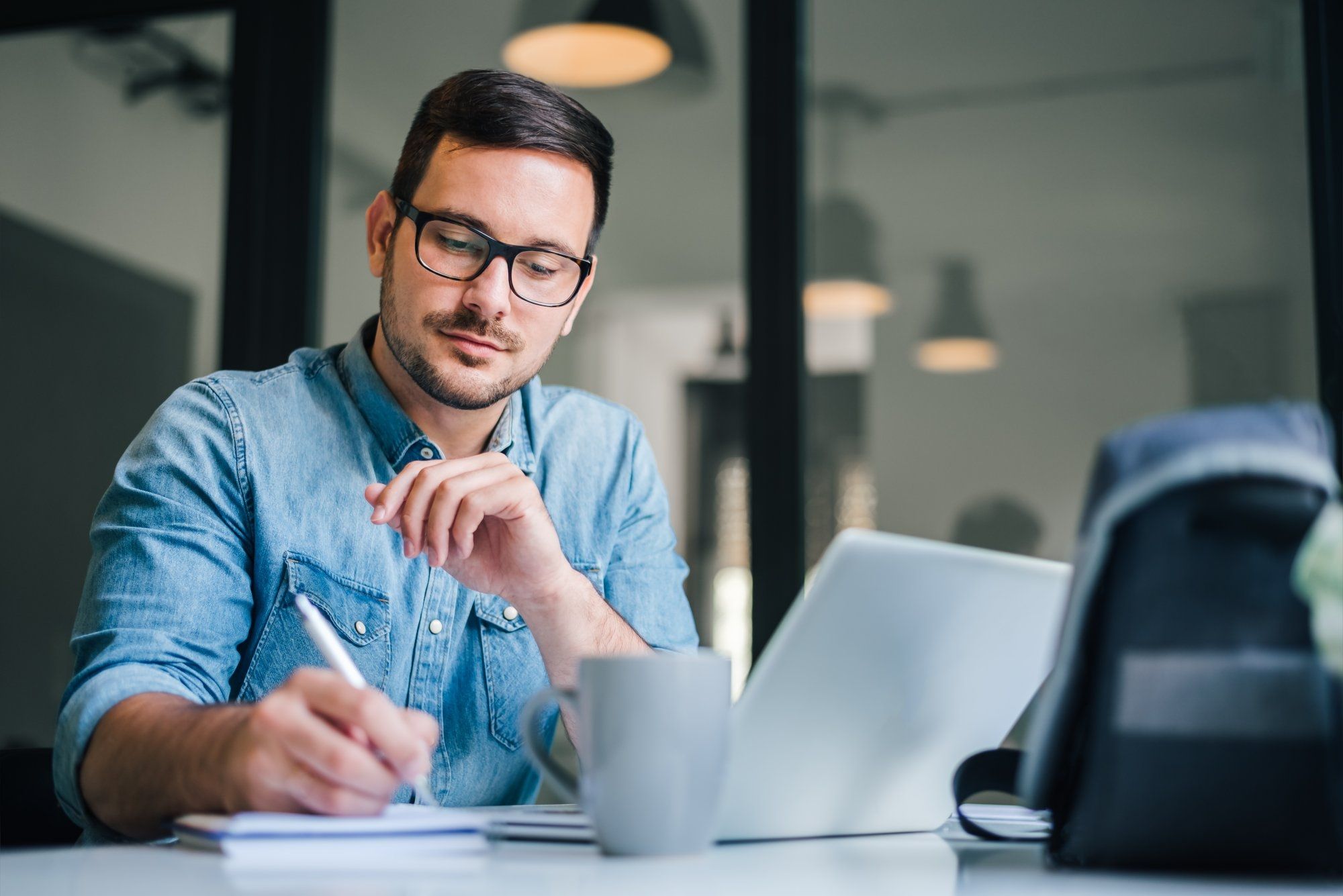 Close up portrait of handsome man working from home office taking reading and writing notes in note 