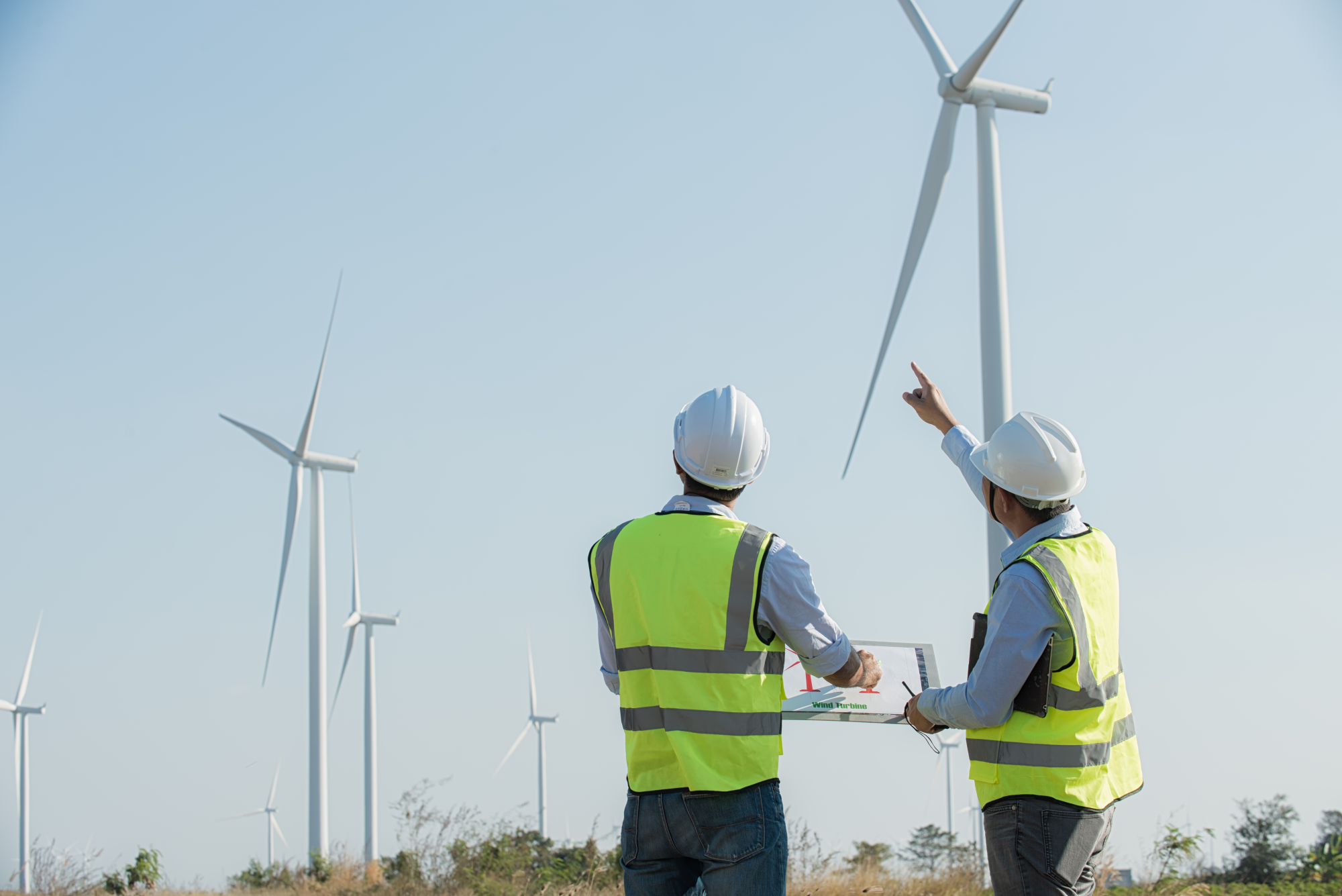 Back view of two engineers discussing against turbines on wind turbine farm