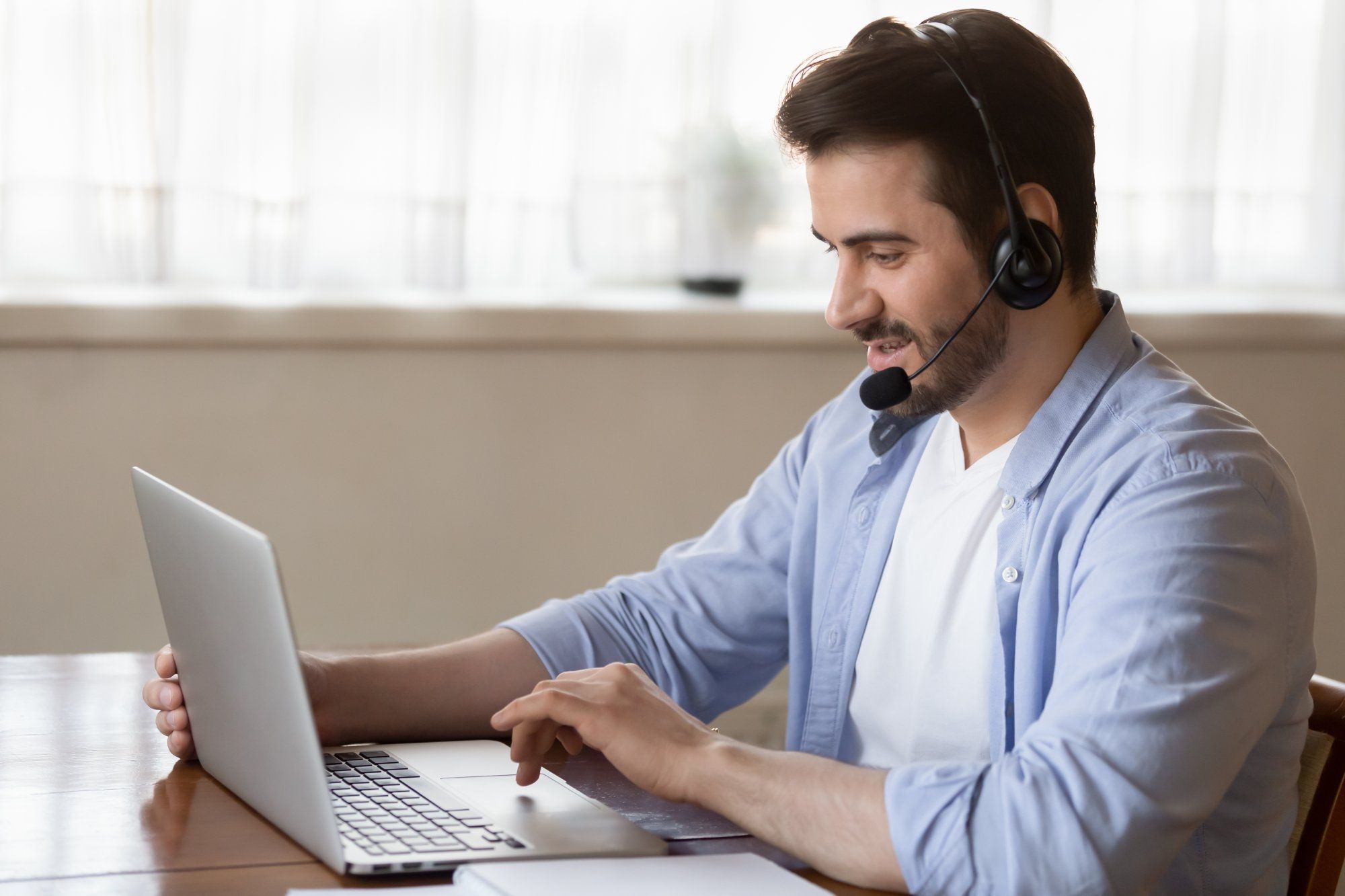 Side view young man wearing wireless headset with microphone, looking at laptop screen, study on onl