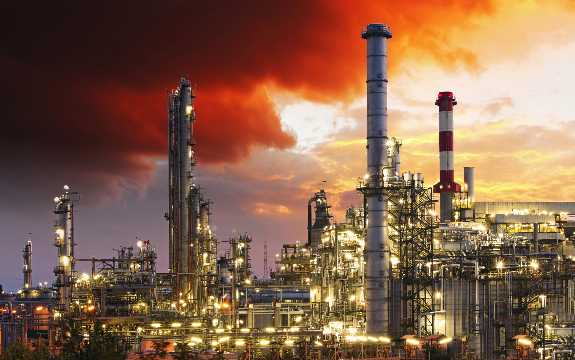Large refinery with tall chimneys and illuminated plant components at dusk