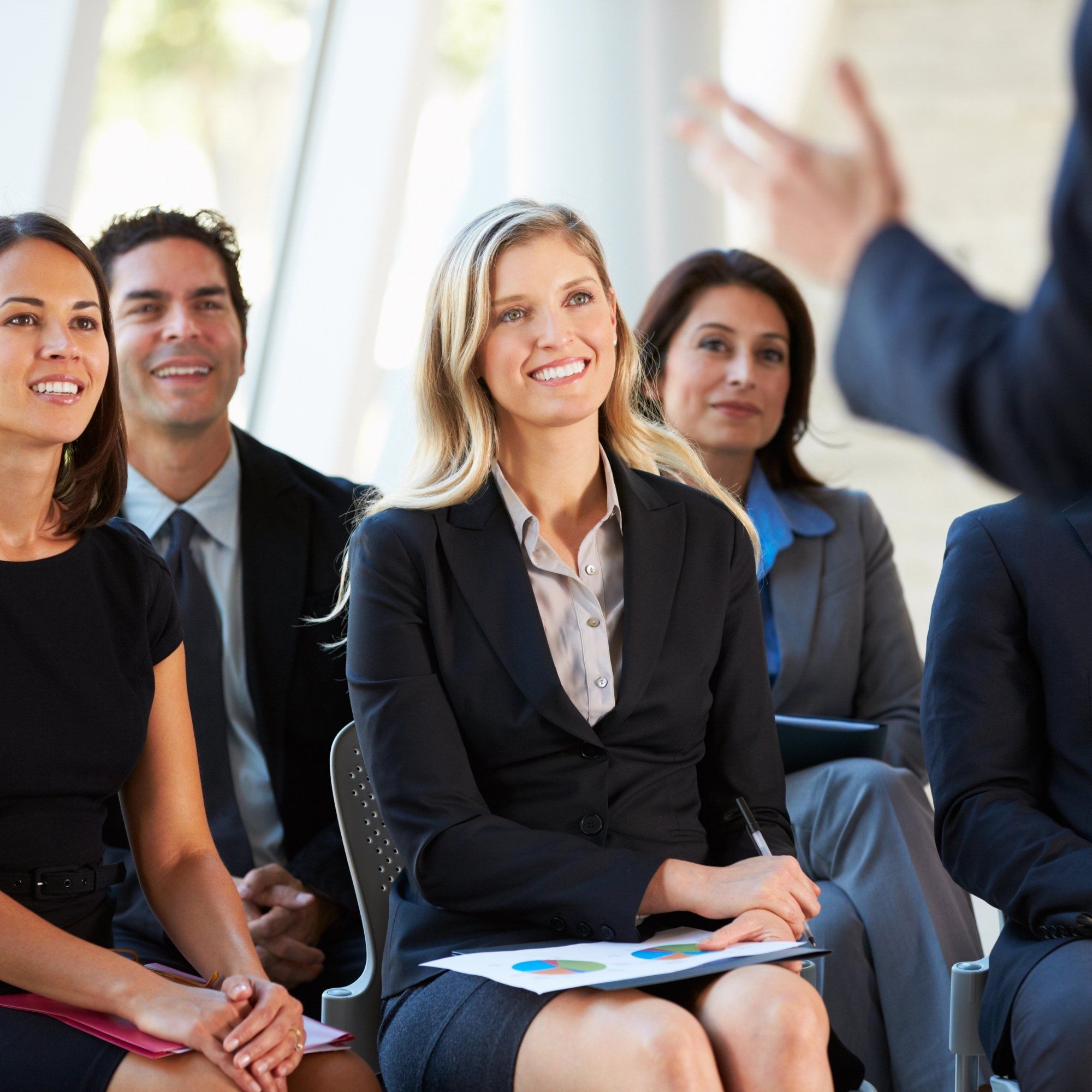 Several participants in a workshop listen to a presentation, the moderator stands with his back to t