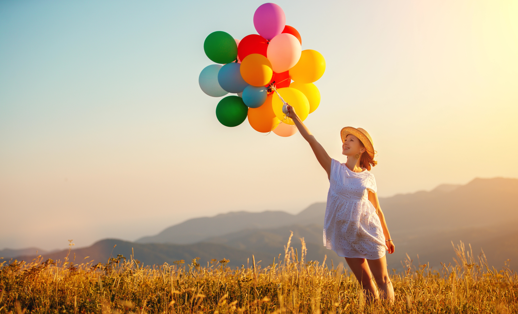 young happy woman with balloons at sunset in summer