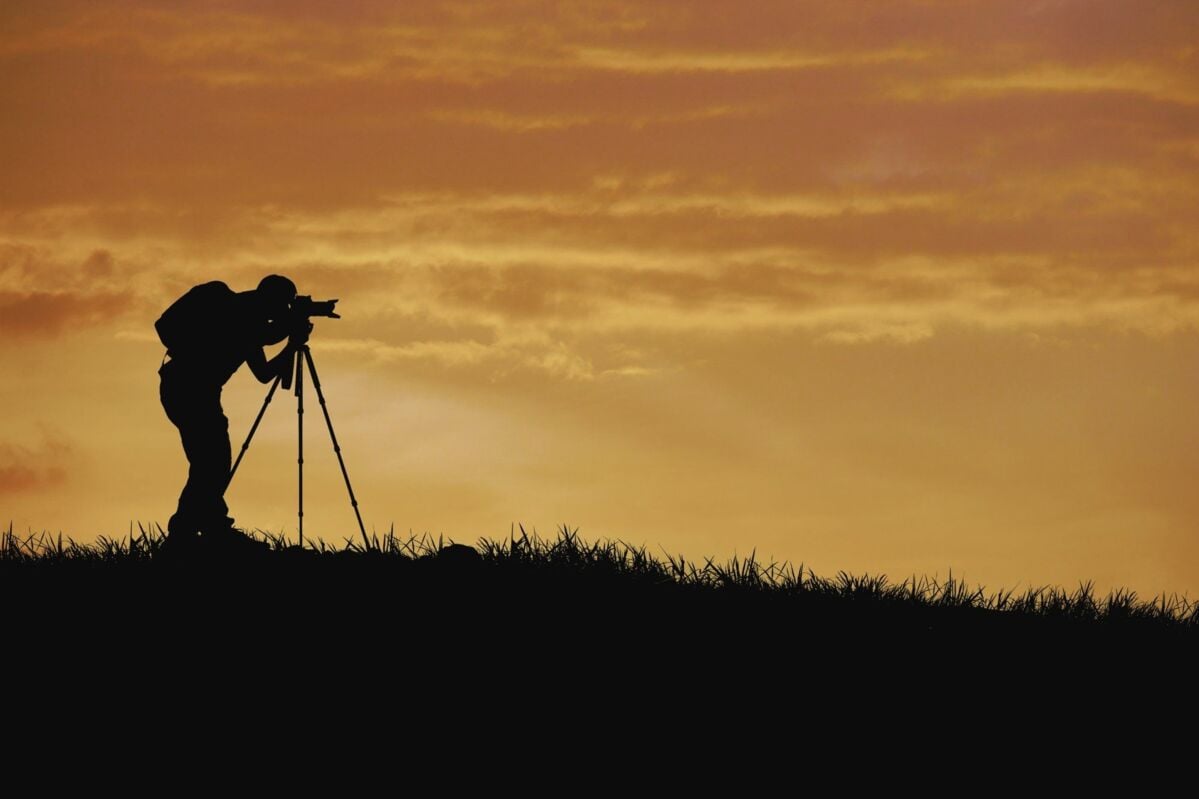Silhouette of a photographer at sunset with camera and tripod – symbolizes observation, documentat