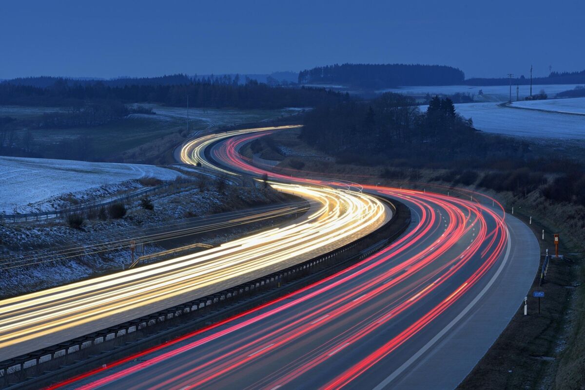 A winding road in the twilight that runs through an open landscape, accompanied by flowing, glowing 