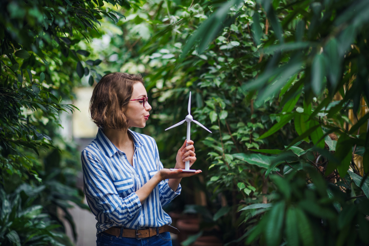 Woman holding a model wind turbine in the middle of a forest.