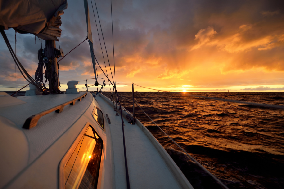 White yacht sailing in an open sea at sunset. A view from the deck to the bow, mast, sails. Epic clo
