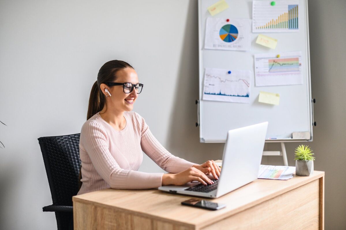 A woman loves her job in an office. A young, attractive woman wearing glasses uses a laptop to work,