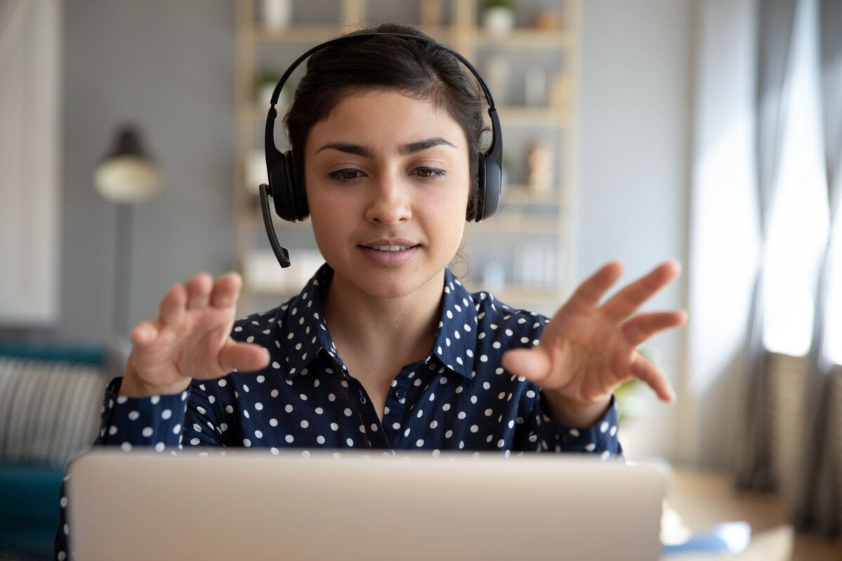 dqs-young woman sits in front of a laptop with a headset and takes part in an online meeting