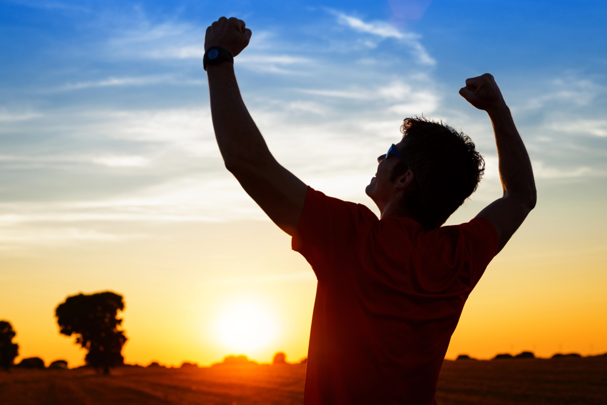 Man raising both arms in the sunset in success