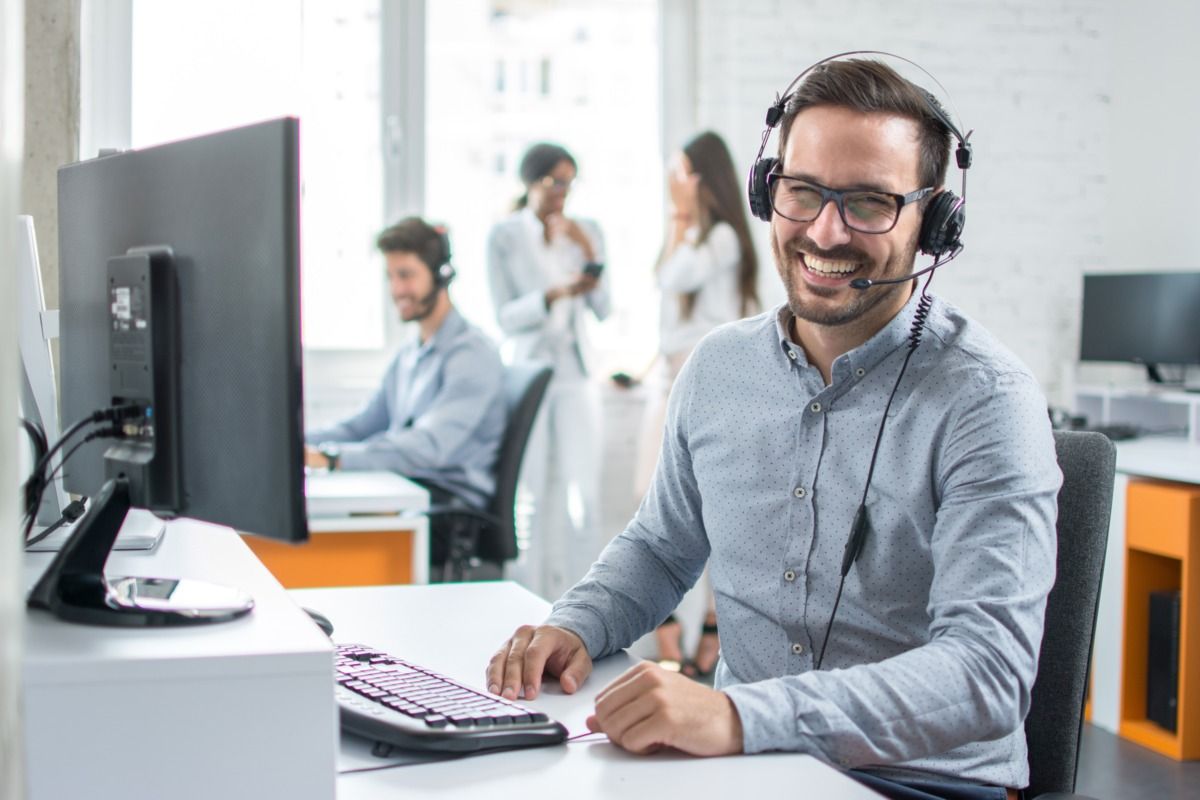 Man with full beard, glasses and headset smiling in a telephone service center