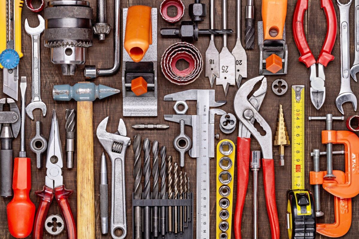 Tools such as hammers, drills, wrenches, calipers, and pliers are neatly arranged on a wooden table.