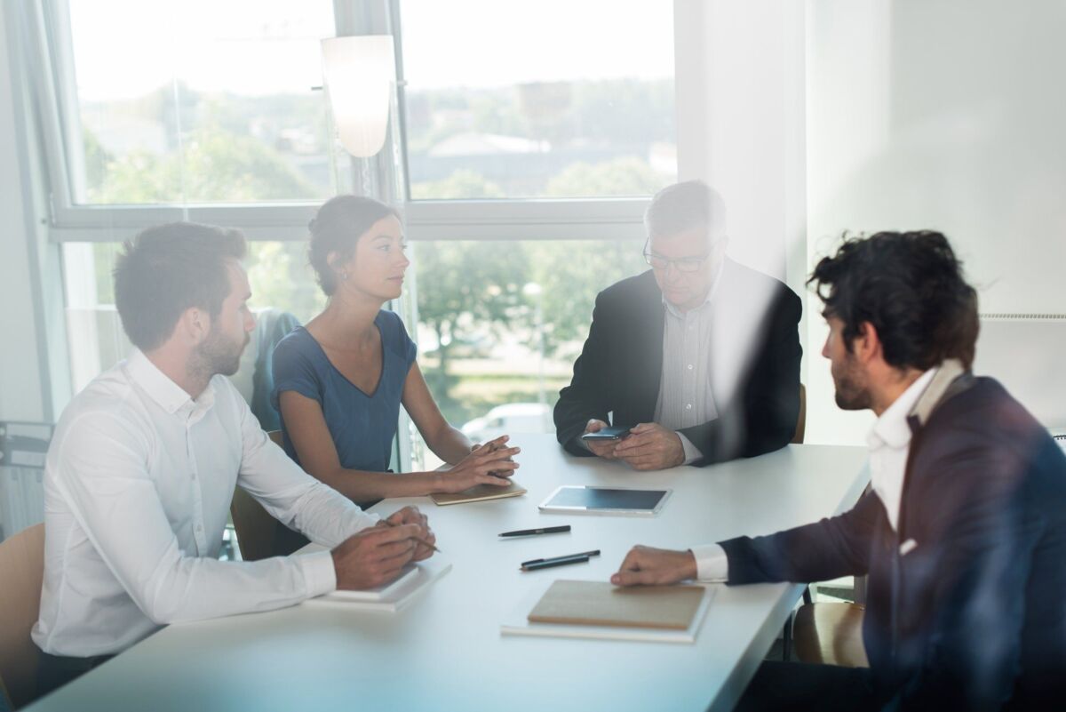 Shot through office window, office business meeting. The team is sitting at a table, brainstorming s