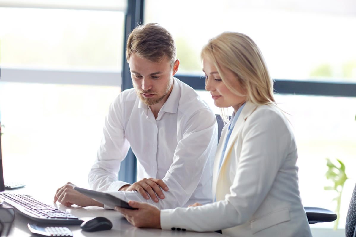 Two young happy businessmen look at documents on a tablet in the office.