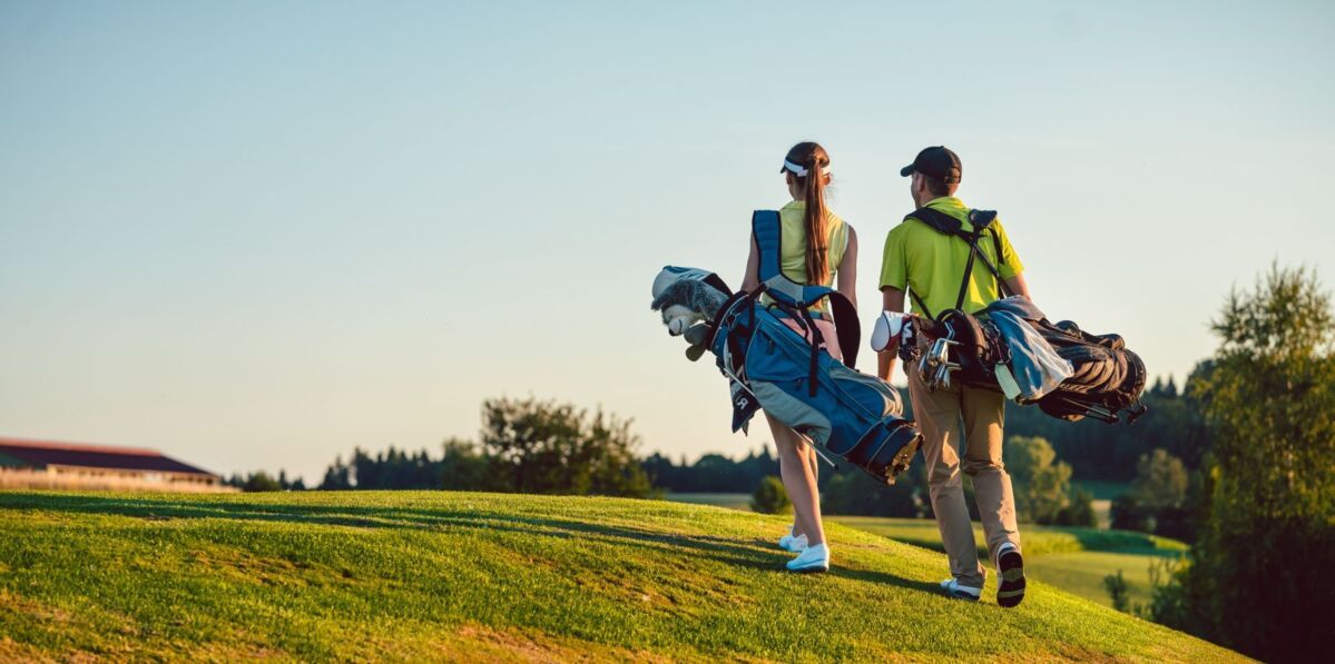 Man and woman walking with their golf bags on the lawn towards the clubhouse on the top left