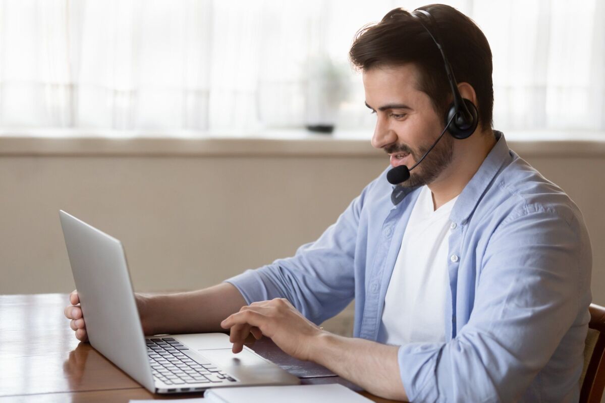 Side view young man wearing wireless headset with microphone, looking at laptop screen, study on onl