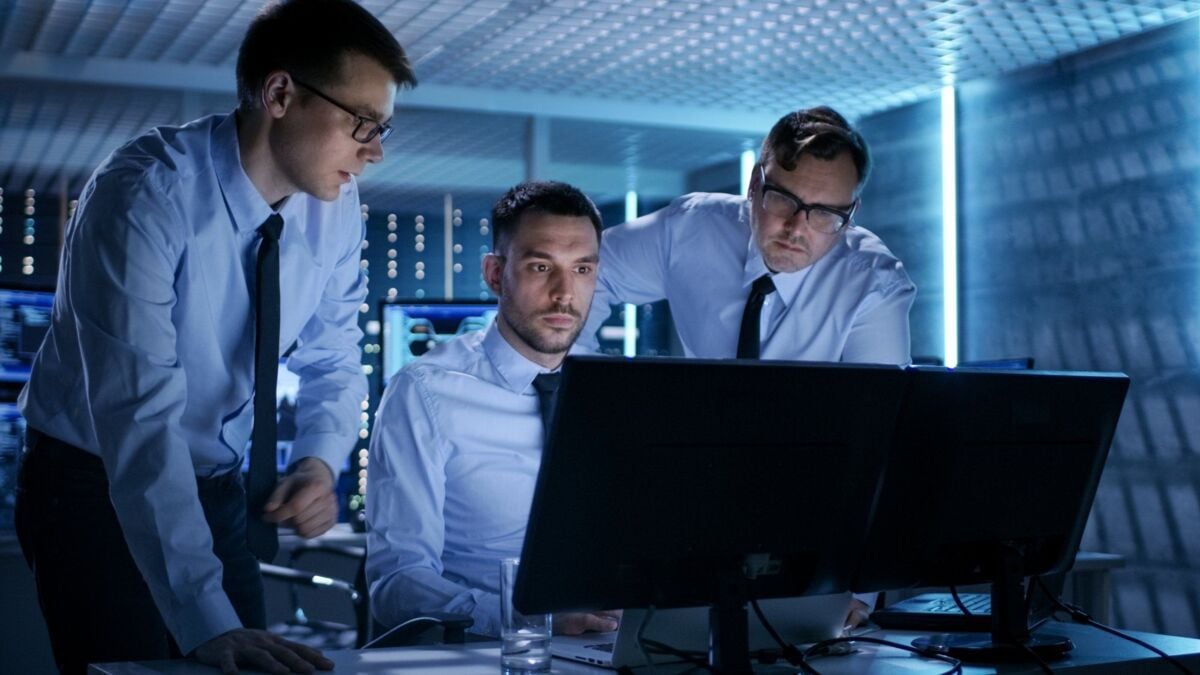 webinar-cyber-security-dqs-it system technicians in a control room look at screens with data