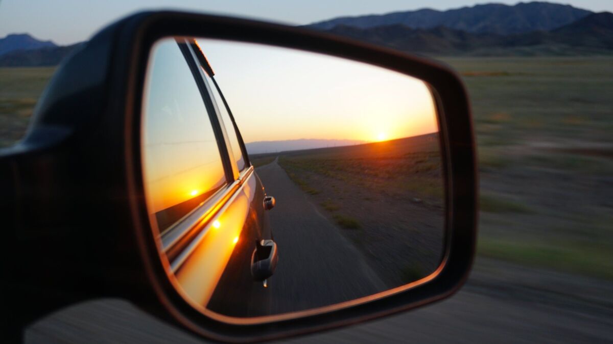 View in the side mirror of the car. Orange dawn over the hills. The car is going at high speed. Gree