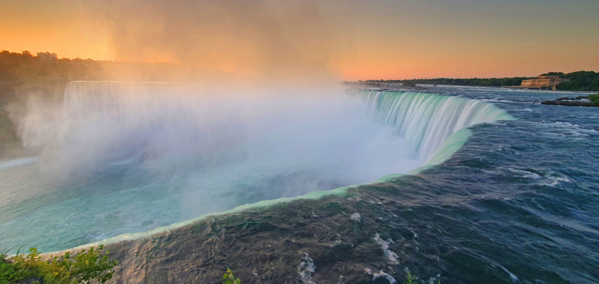 A breathtaking view of Niagara Falls in the warm light of sunset – mist rises and catches the ligh