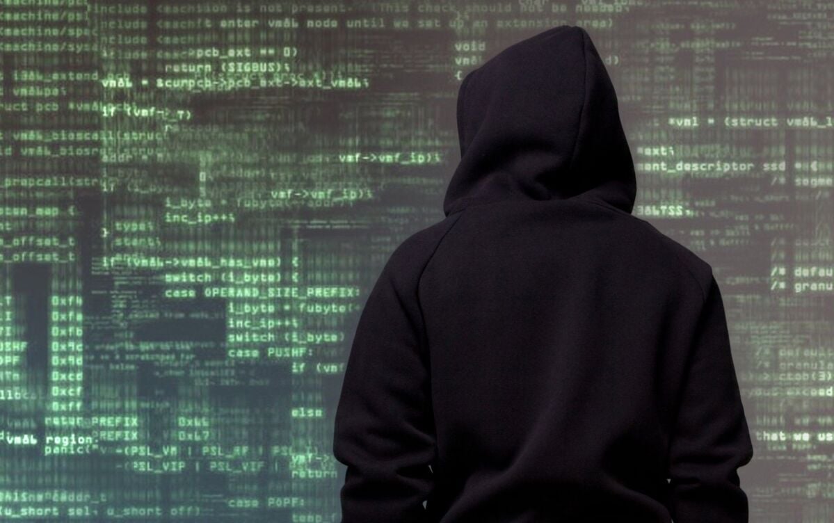 it-security-kmu-dqs-a person in the typical black hoodie of a hacker stands with his back to the vie