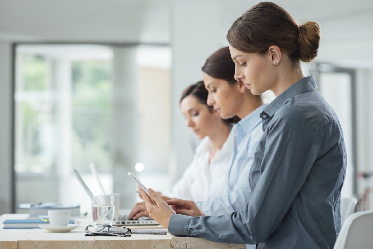 dqs-three businesswomen work at desk with smartphone and laptop