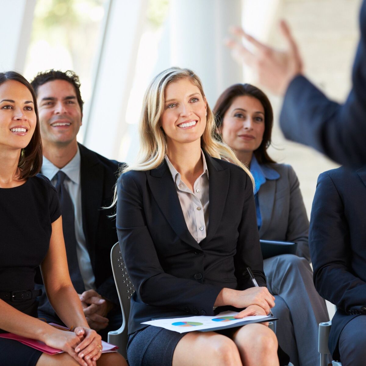 Several participants in a workshop listen to a presentation, the moderator stands with his back to t