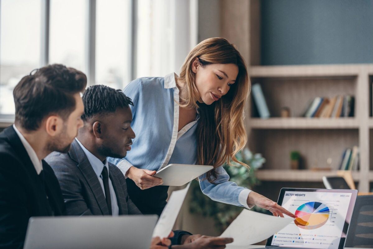 Three confident business people analyzing marketing data and using laptop while working in office to
