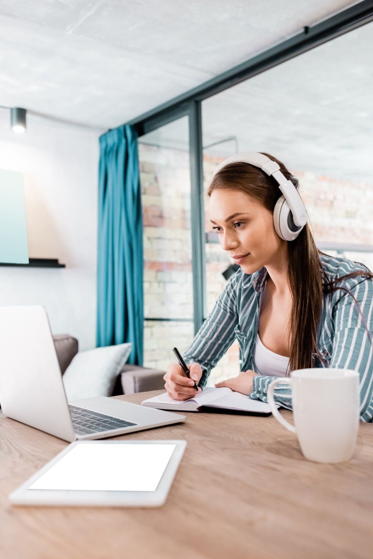 Young woman with laptop and headphones taking an online class at her desk