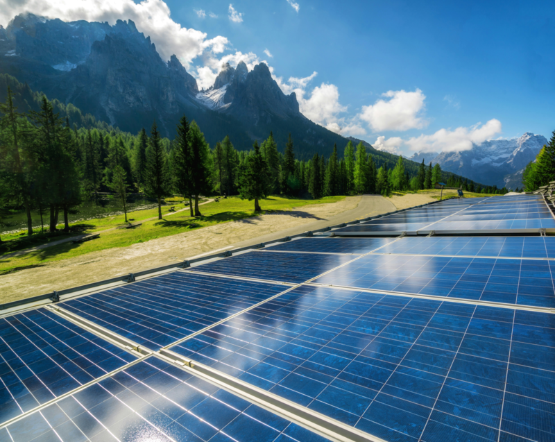 A field of solar panels amid a conifer forest and mountains