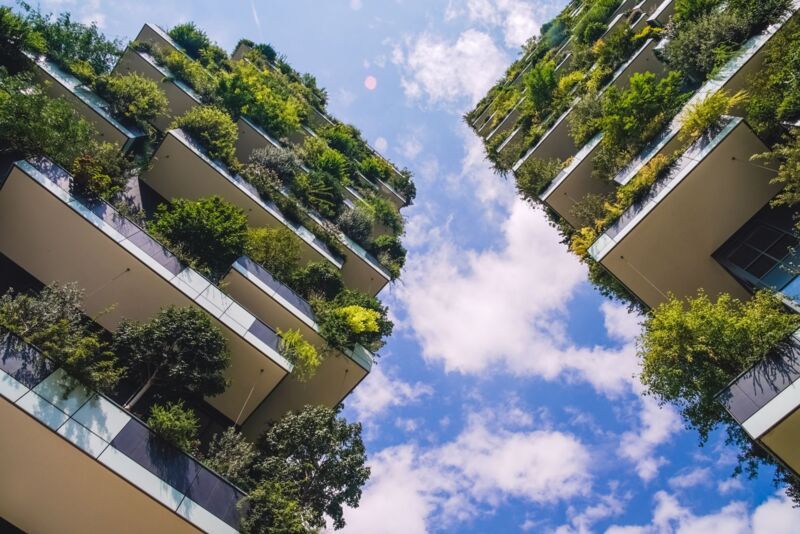 umweltleistung-iso14001-dqs-zwei nebeneinander stehende hohe mehrstoeckige wohngebaeude mit stark begruenten balkonen ragen in den blauen himmel
