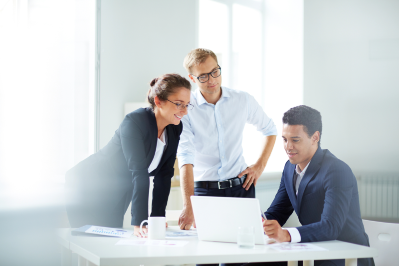 Three businessmen look at documents on a laptop in the office.