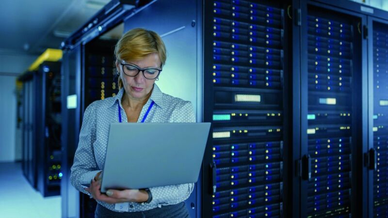 Portrait of a blonde woman with glasses working on her laptop in the computer centre, server cabinet