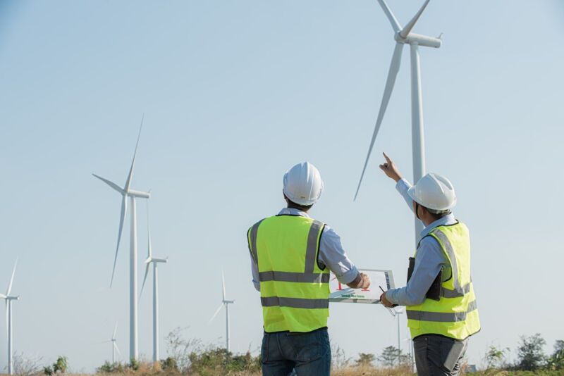 Back view of two engineers discussing against turbines on wind turbine farm