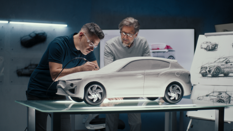 Two experienced automotive engineers discuss the car design looking at the sketches on the board. Ma
