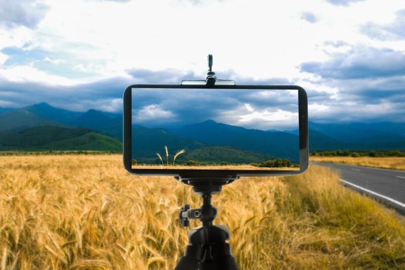 Taking photo of beautiful wheat field with smartphone mounted on tripod