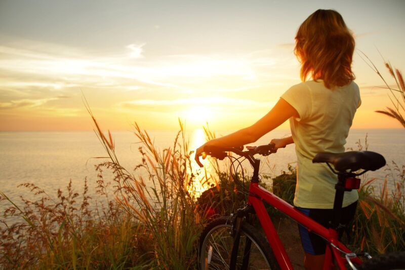 Person with bicycle at a lake looking into the sunrise