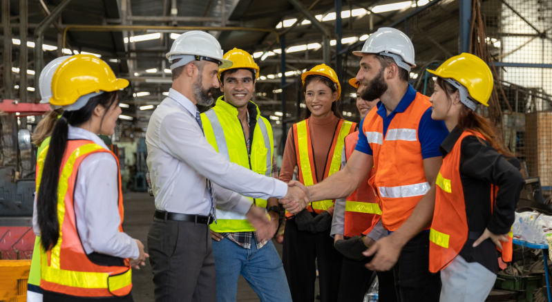 dqs-businessman shakes the hand of a man in protective clothing surrounded by other employees in wor