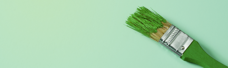 a green paintbrush with some green paint, on a pale green background with some blank space on the le