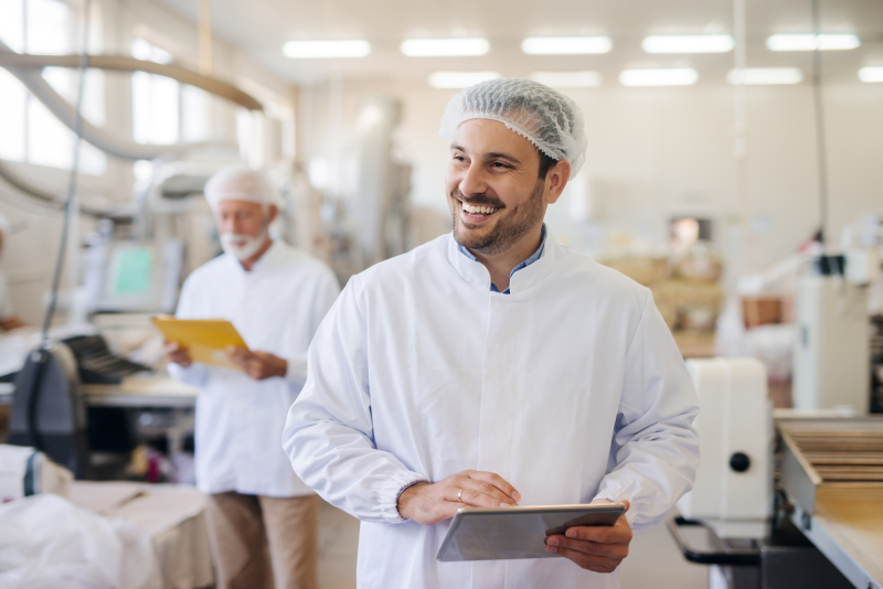 Smiling man using tablet while standing in food factory.